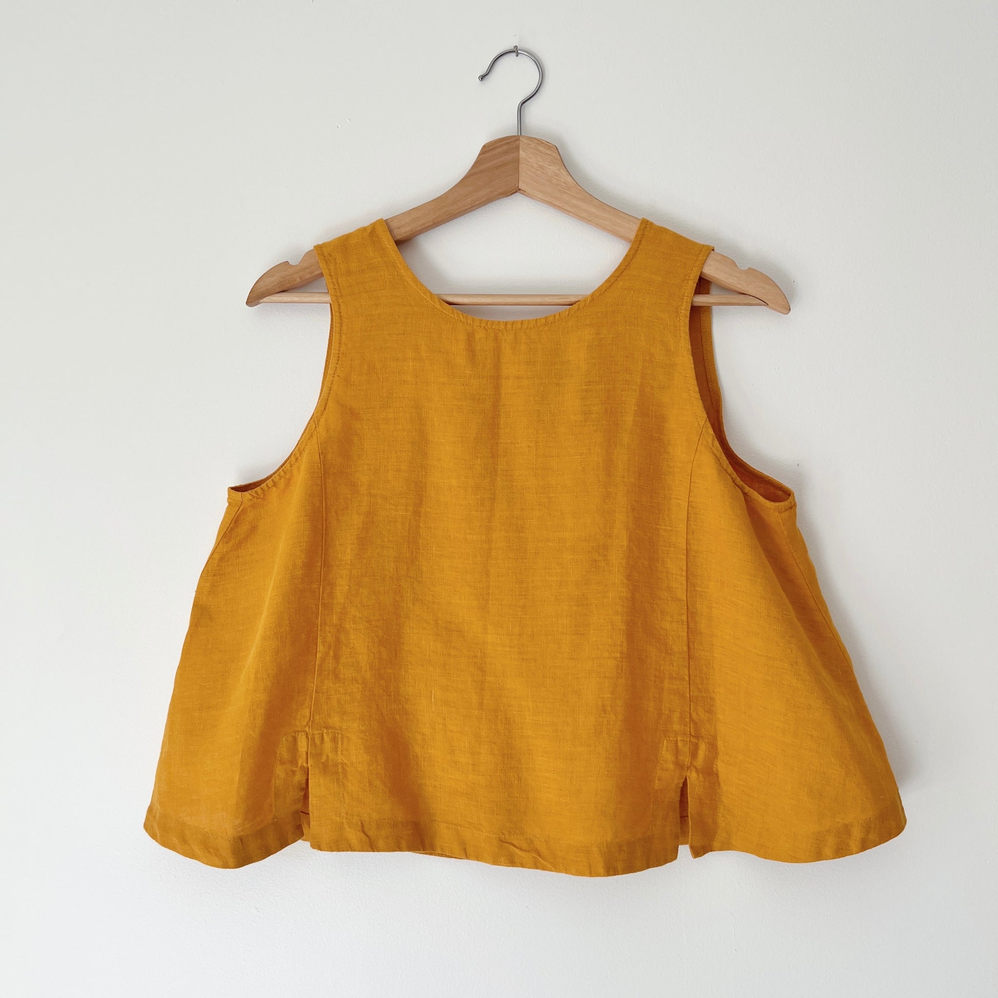 Yellow sleeveless top on a wooden hanger against a white background