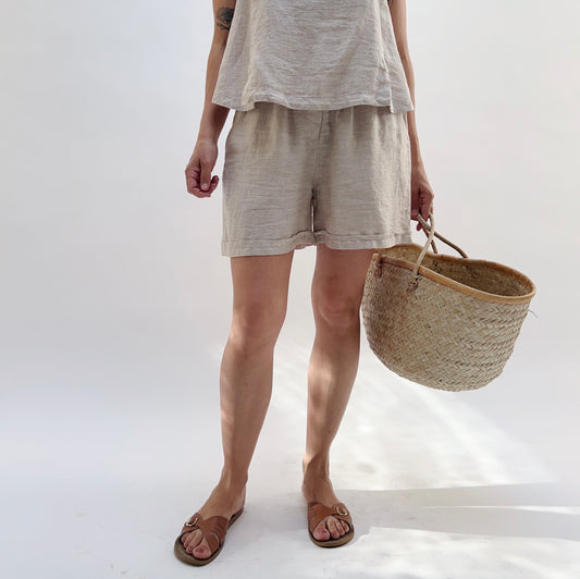 Person wearing a gray t-shirt and shorts holding a woven basket on a white background