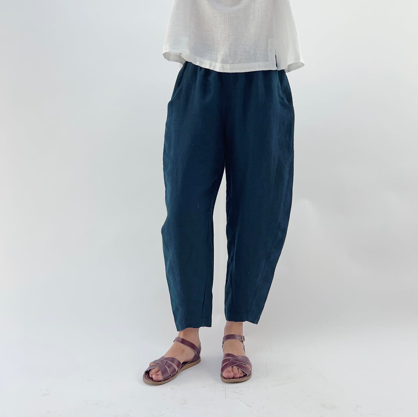 Person wearing navy linen pants and a white linen top on a plain background. They are wearing purple sandals.
