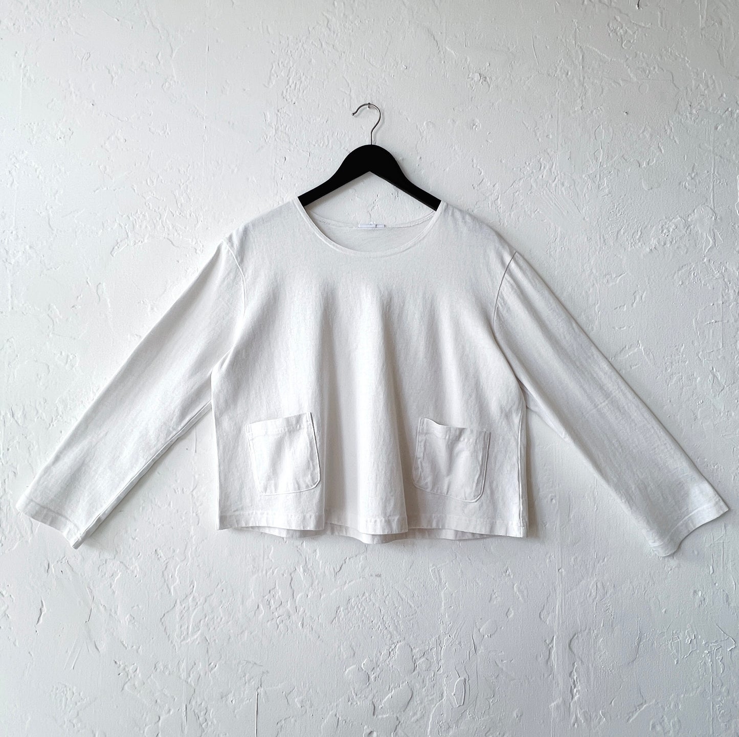 White long-sleeve crop top on a hanger against a white wall