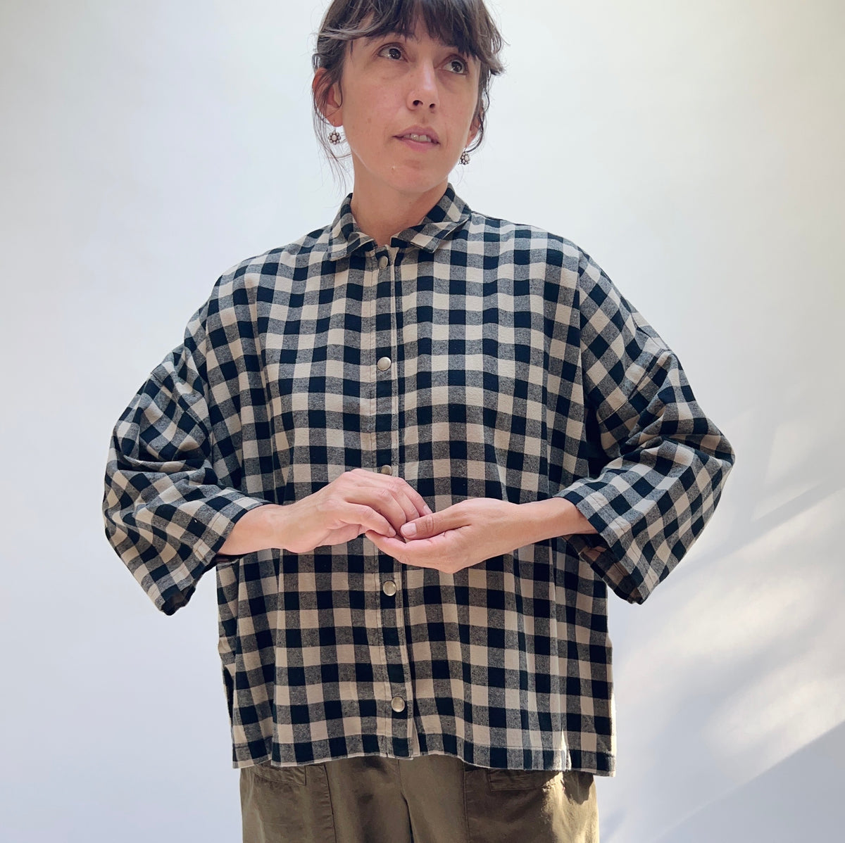 Model wearing the Eleven Stitch Big Check Big Shirt in Fennel, front view, oversized black and tan gingham cotton shirt with snap buttons and chest pocket, styled with olive trousers
