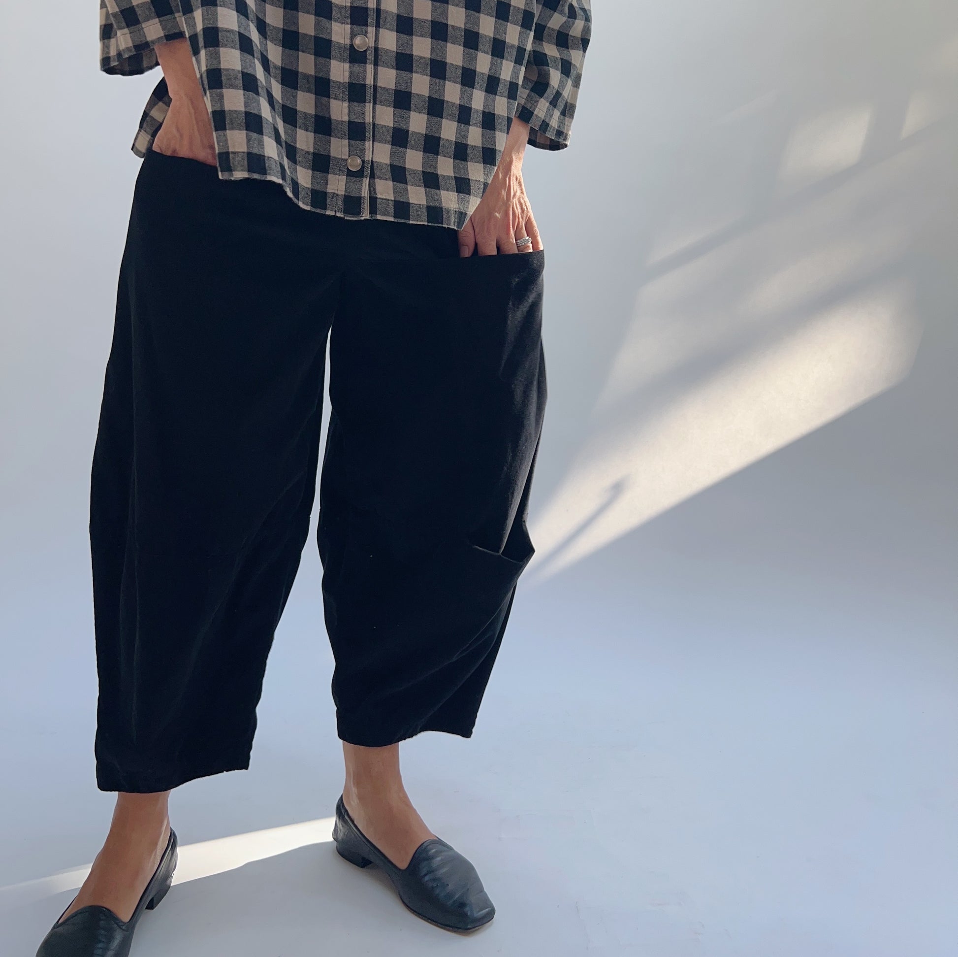 Model with hand in side pocket of black corduroy pant, highlighting the functional pocket placement and cropped length

