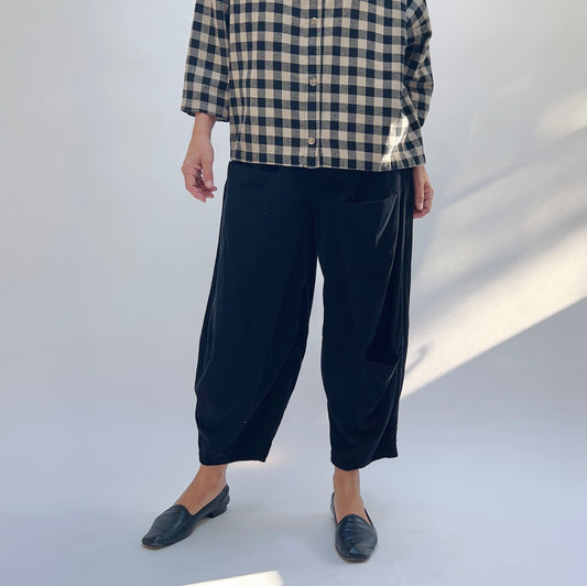 Front view of model wearing black corduroy cropped pants with relaxed fit, paired with a plaid shirt and black loafers