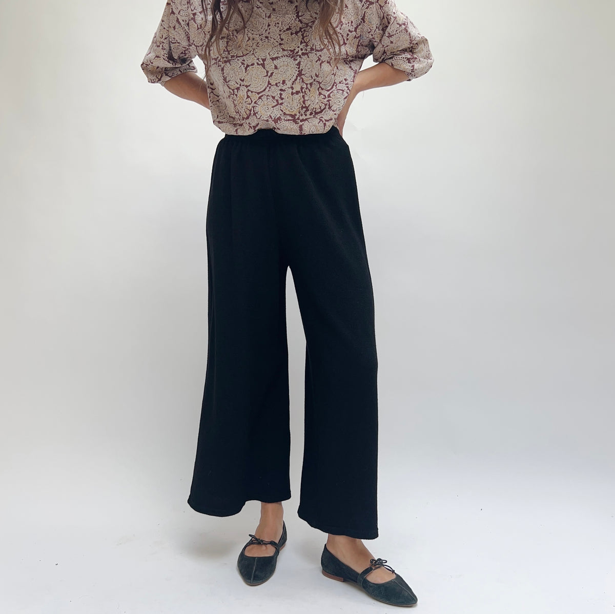 Cut Loose Marled Knit Crop Pant in Black, front view, wide-leg silhouette with elastic waistband, worn with a floral blouse and black ballet flats
