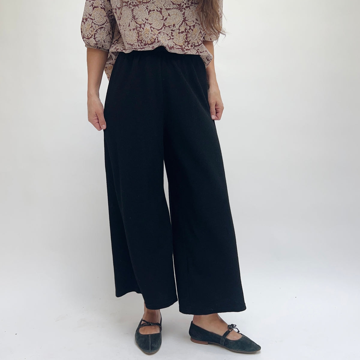 Cut Loose Marled Knit Crop Pant in Black, front view showing full-length wide leg and elastic waistband, styled with a floral blouse and black ballet flats
