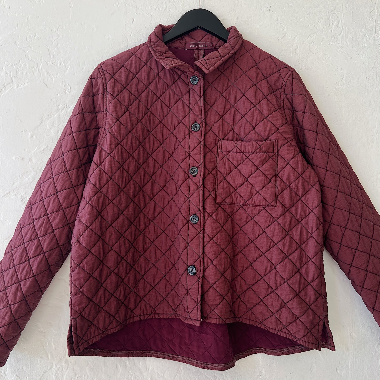 Quilted maroon jacket with a diamond pattern on a hanger against a white wall