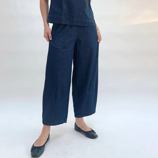 Person wearing dark blue wide-leg pants and flat shoes on a white background