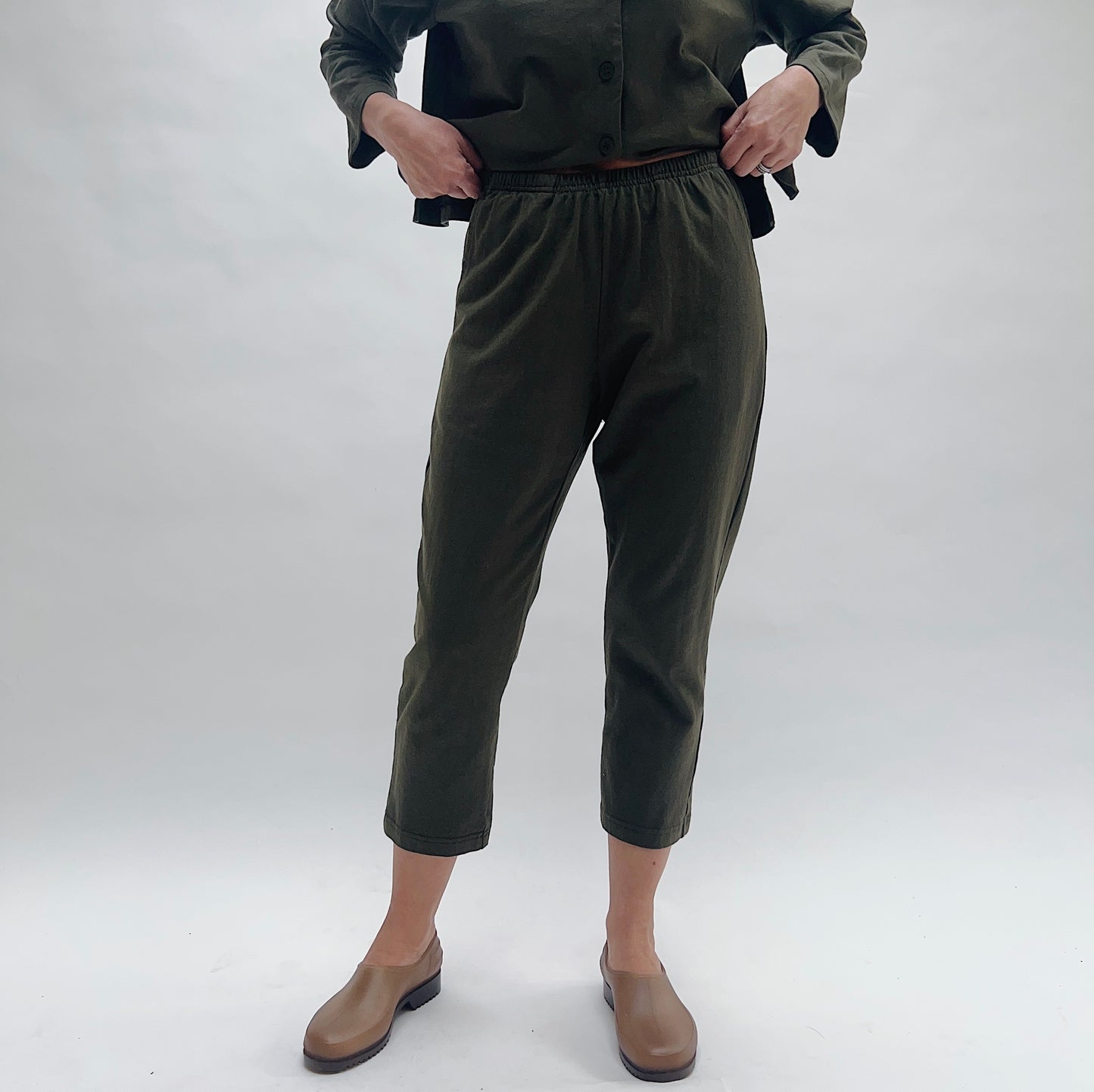 Person wearing olive green pants and brown shoes on a white background