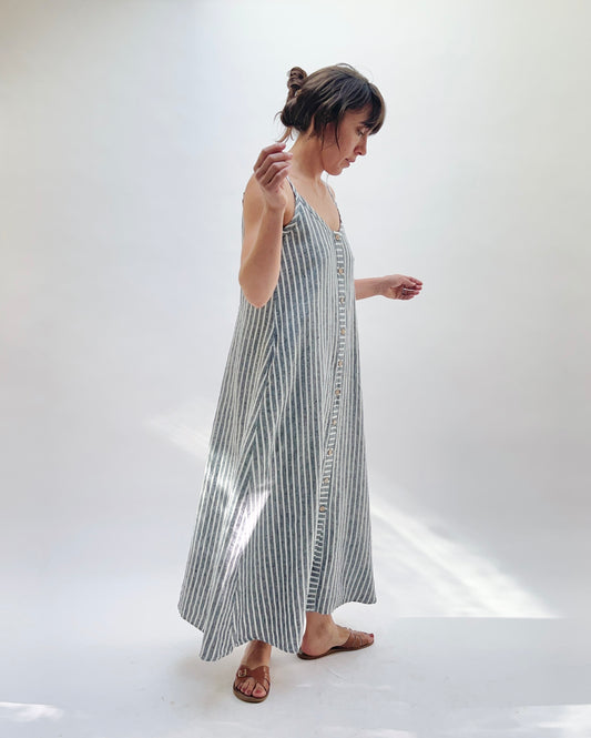 Woman wearing a long, striped linen dress in white and grey on a white background.