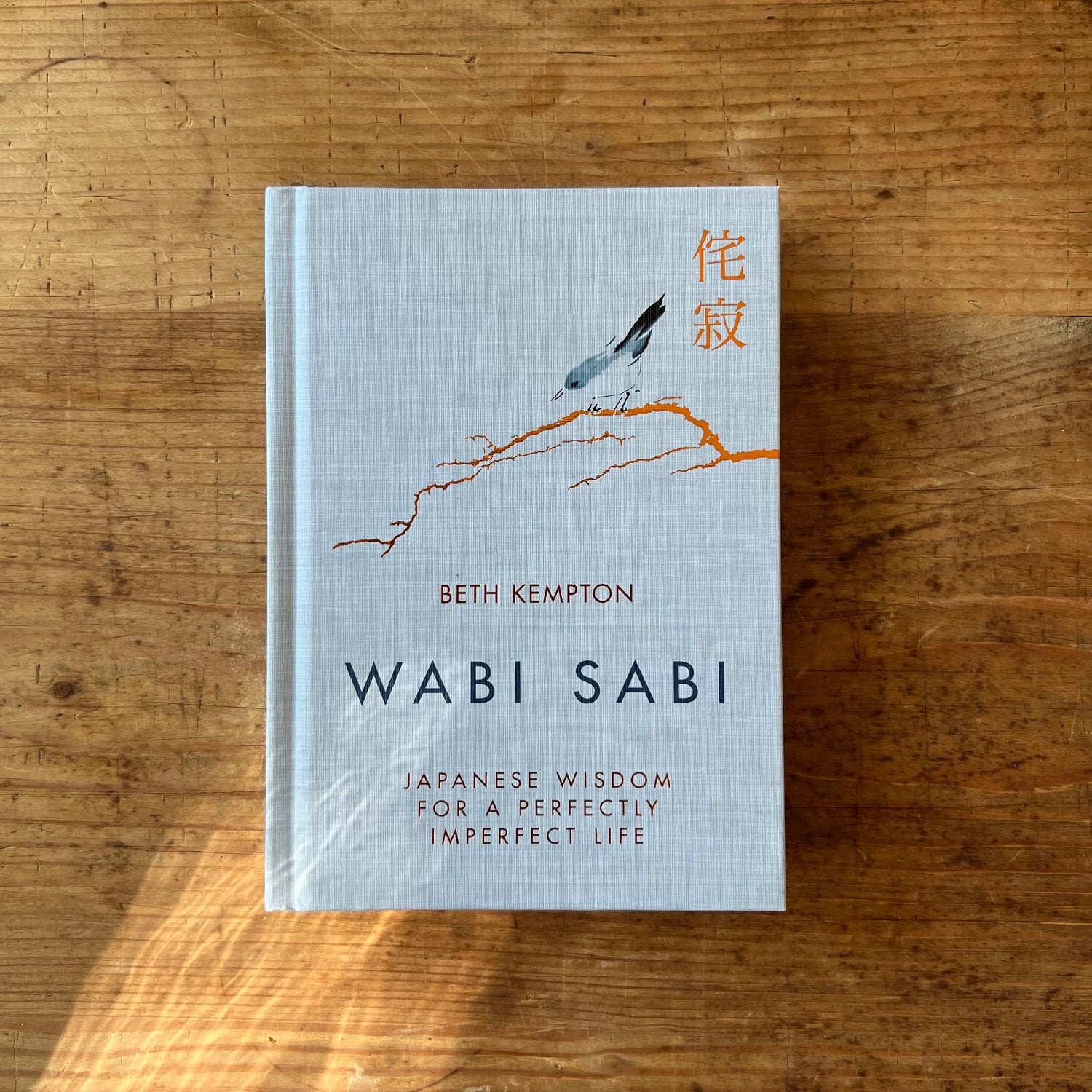 Front cover of Wabi Sabi by Beth Kempton, a pale grey hardcover featuring a watercolor bird perched on an orange branch, with Japanese characters in orange and the subtitle Japanese Wisdom for a Perfectly Imperfect Life
