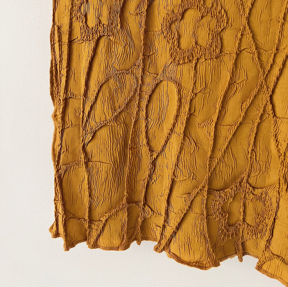 Close-up of the mustard crinkle top's hem, showing the raised, puckered fabric texture.
