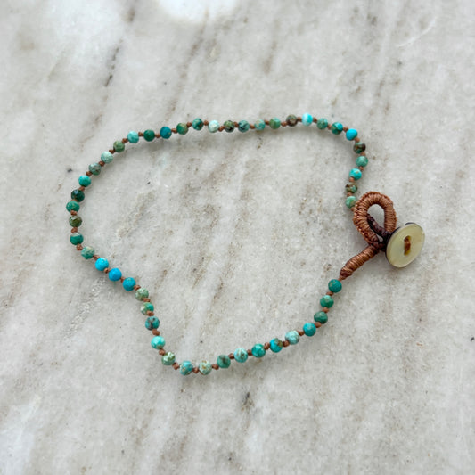 A faceted turquoise beaded bracelet with a hand-knotted, waxed silk cord and a mother of pearl button closure.
