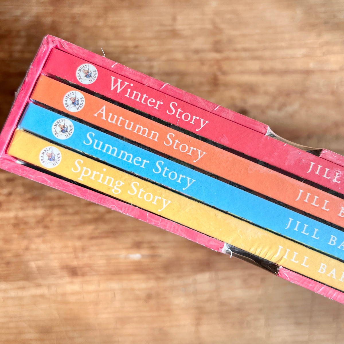 Close-up of the four book spines inside the slipcase: Winter Story in pink, Autumn Story in orange, Summer Story in blue, and Spring Story in yellow.
