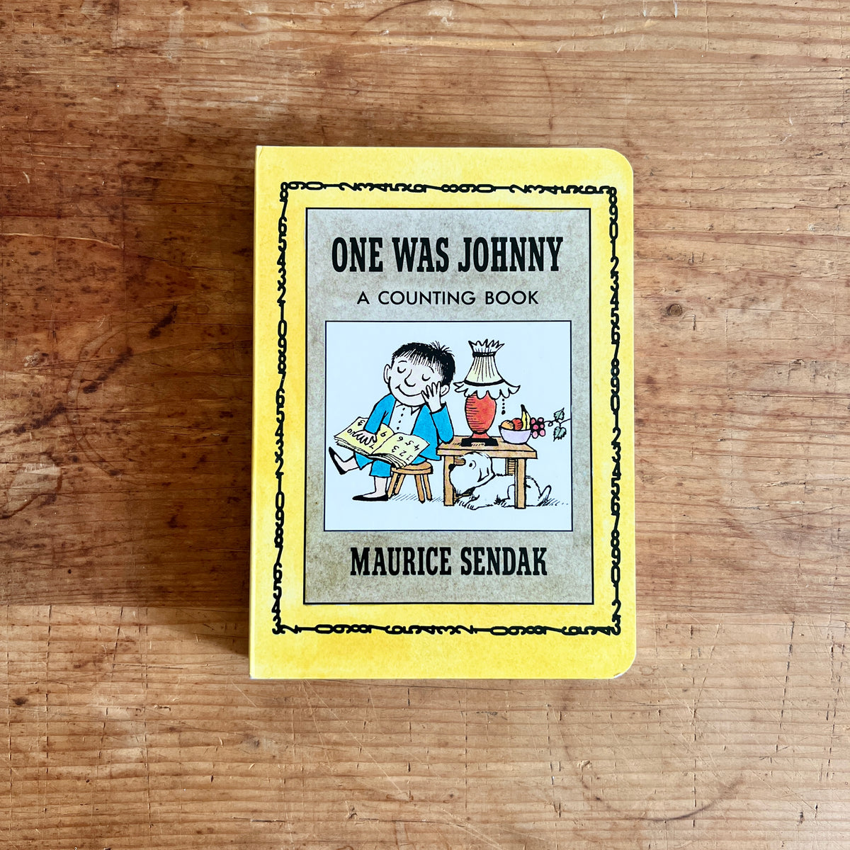Yellow cover of One Was Johnny: A Counting Book by Maurice Sendak, showing Johnny reading beside a table with a dog underneath.
