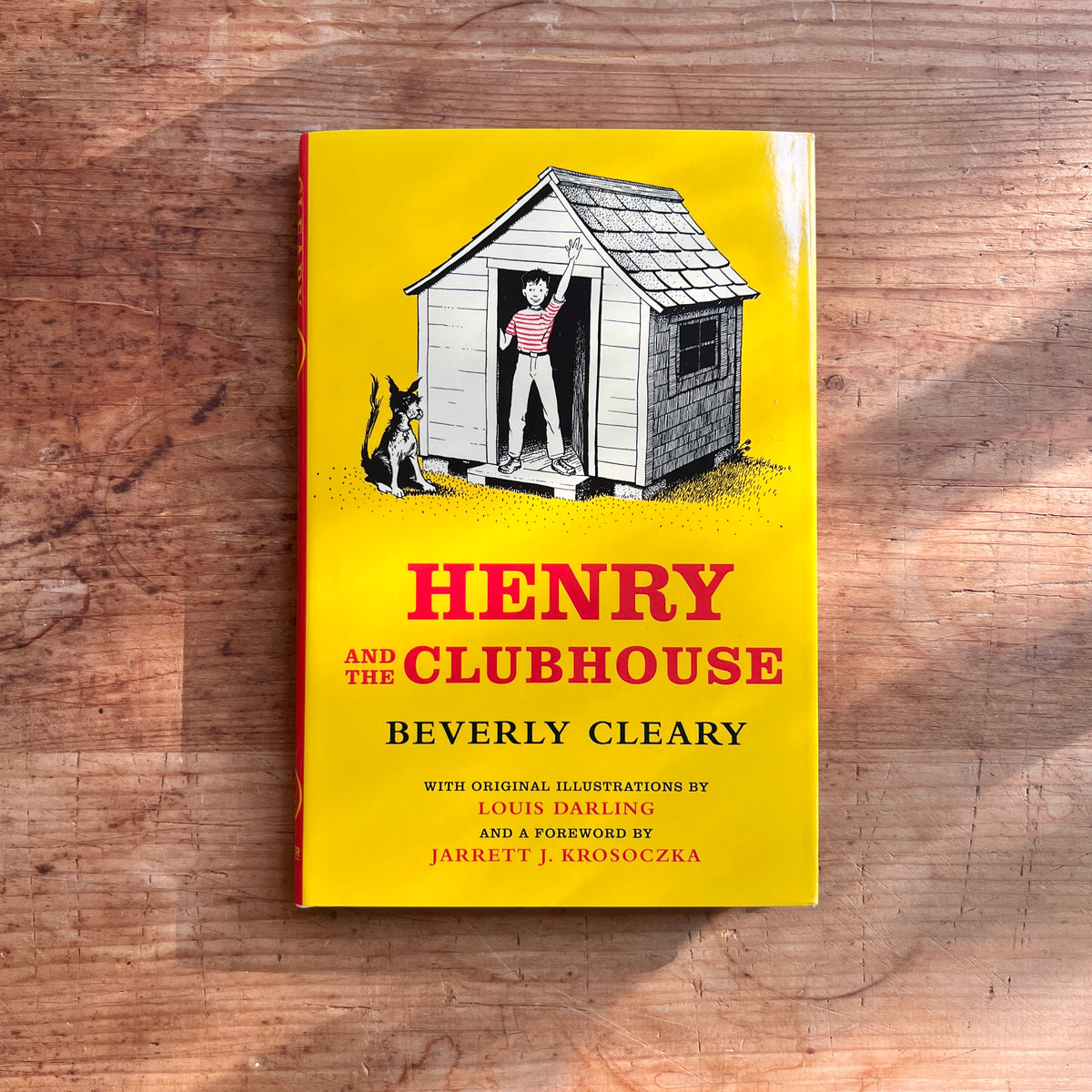 Yellow cover of Henry and the Clubhouse by Beverly Cleary, showing Henry waving from a wooden clubhouse doorway with Ribsy sitting outside.
