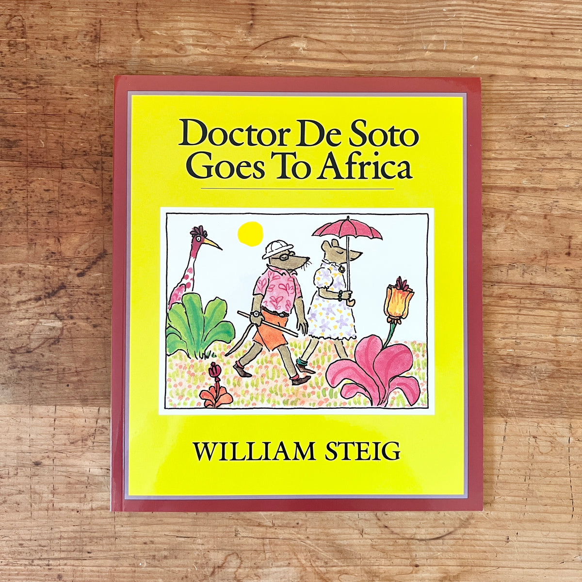 Yellow cover of Doctor De Soto Goes to Africa by William Steig, showing two mice walking among flowers, on a wooden table.
