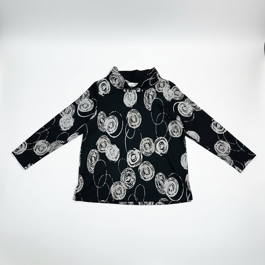 Christopher Calvin Knit Mock Neck Top in Circle Print on hanger, front view showing white crosshatch-textured concentric circle woven jacquard motifs on black, folded mock neck collar, long sleeves, and relaxed A-line silhouette
