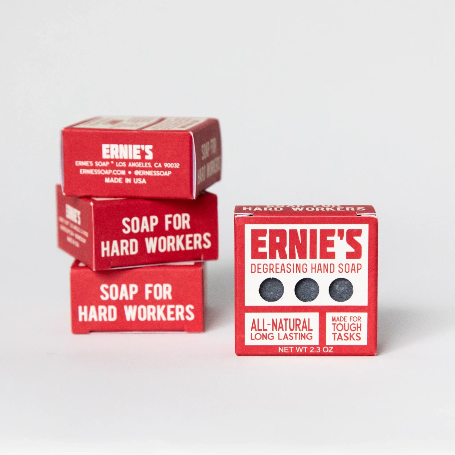 Three red boxes of Ernie's Hard Workers soap bars arranged on a light gray studio background, with one box open to show the dark soap bars inside and another box beside it labeled 'Degreasing Hand Soap'.