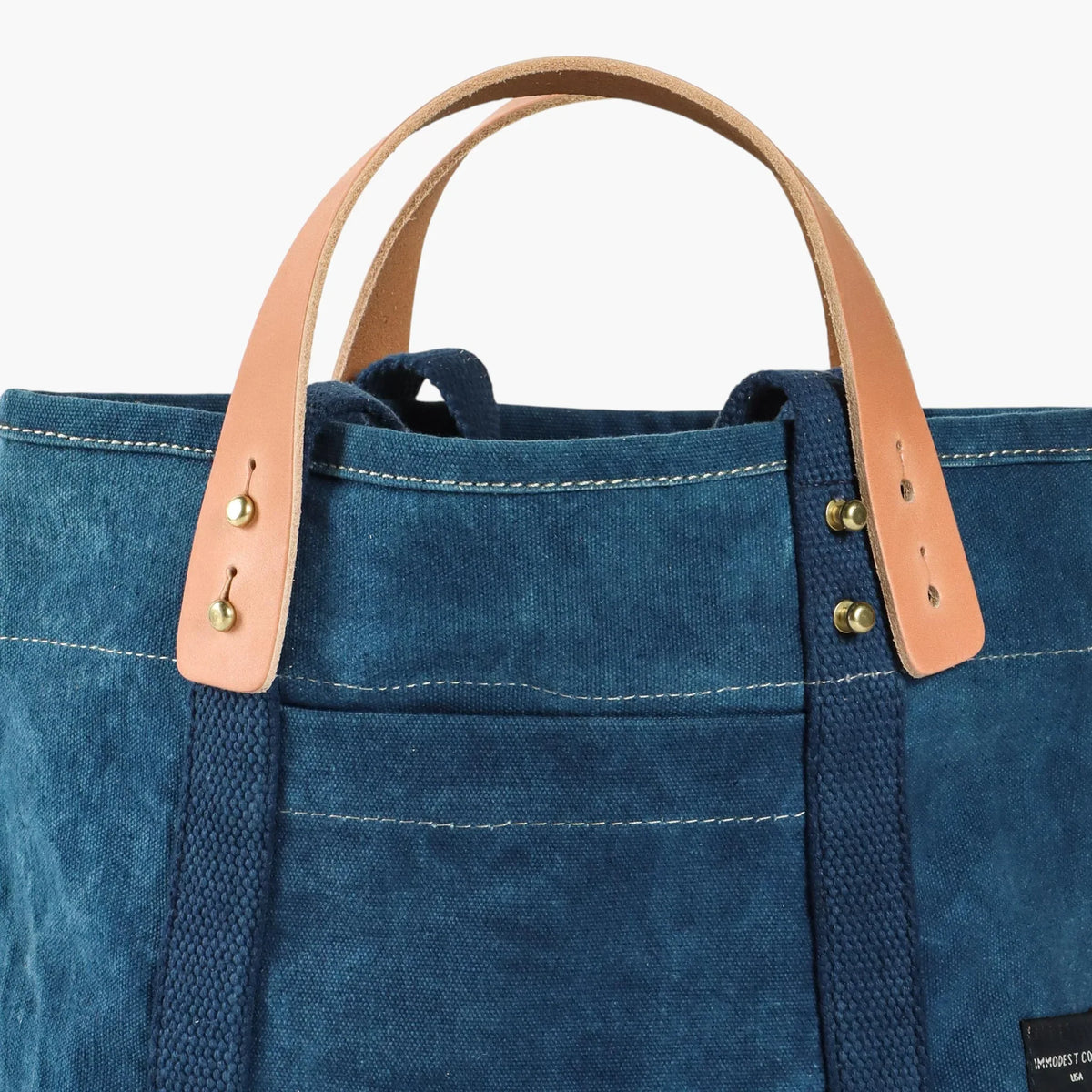 Close-up of the indigo Lunch Tote's removable leather handles, metal buttons, and front pocket.
