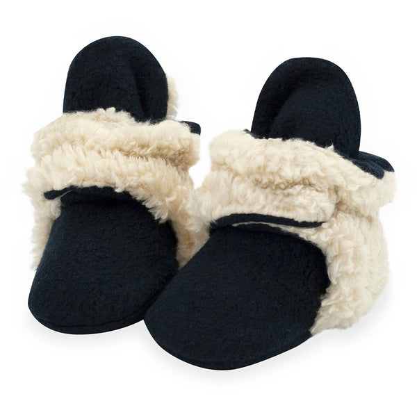 Pair of black Zutano Cozie Furry baby booties with cream faux fur trim and wraparound ankle straps.
