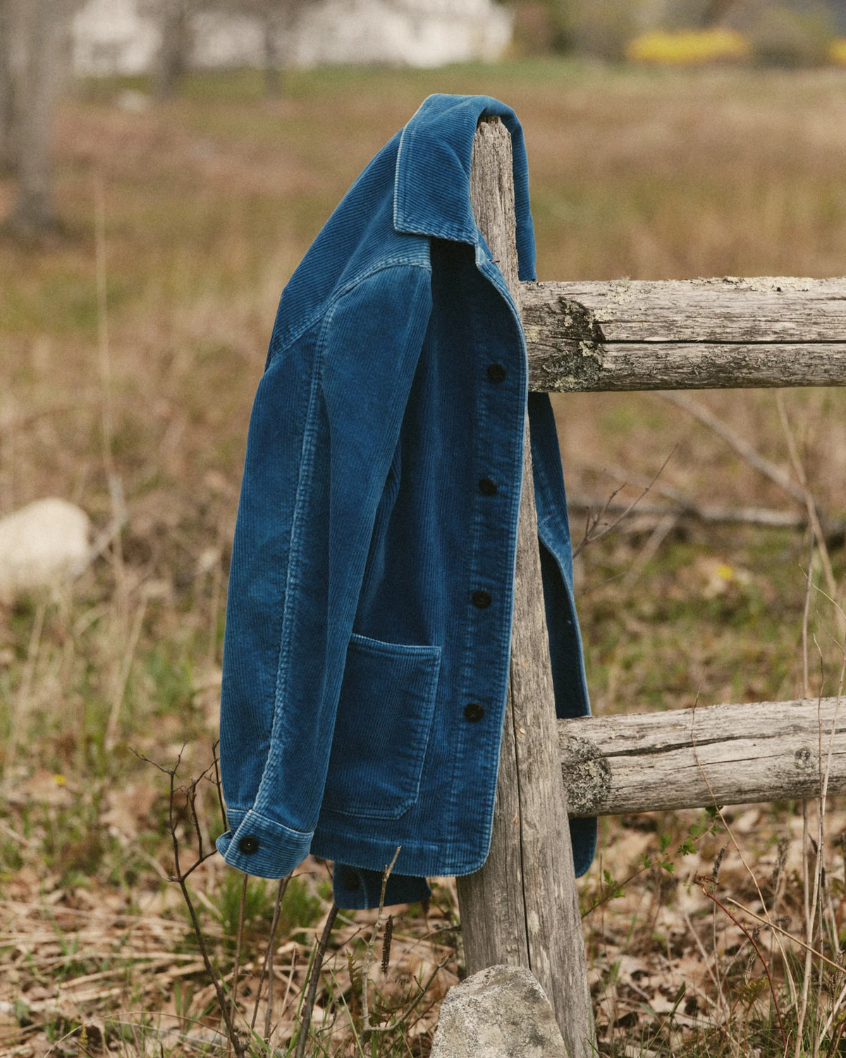 Ojai Jacket in Washed Indigo Corduroy draped over a wooden fence post, showing the collar, sleeve, and lower patch pocket.
