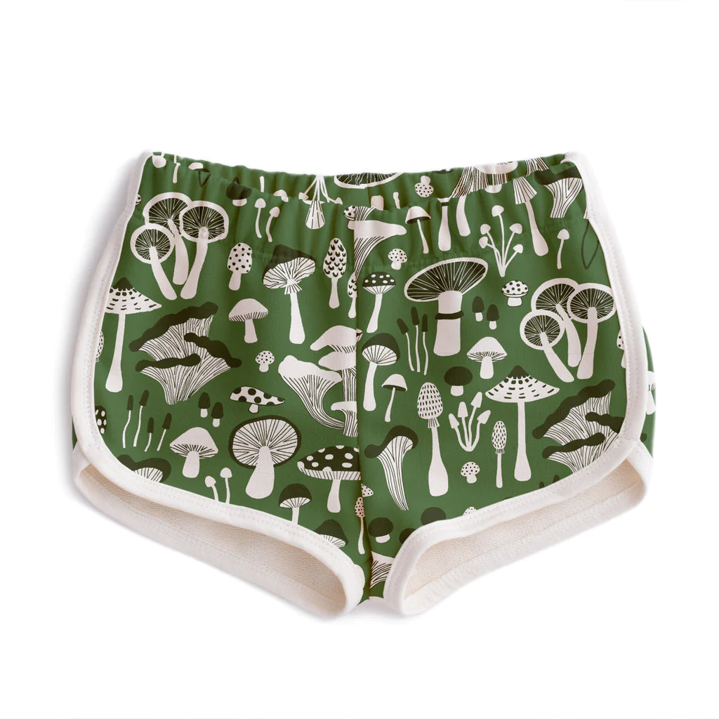 Front view of Winter Water Factory Terry Shorts in Green Fungi Print, showing vintage-inspired runner silhouette with soft elastic waistband, cream contrast piping along leg openings, and an all-over white and dark mushroom illustration print on forest green 100% organic cotton french terry
