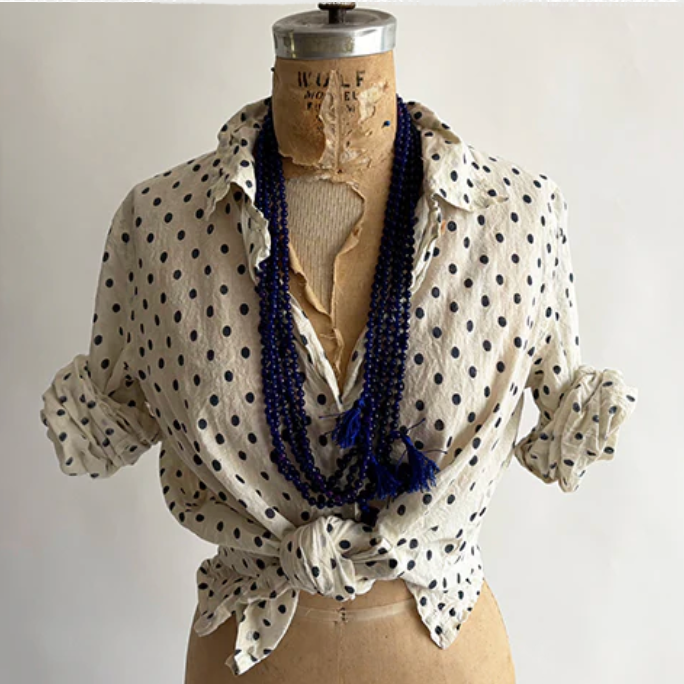 Mannequin wearing a polka dot blouse with a blue scarf on a plain background