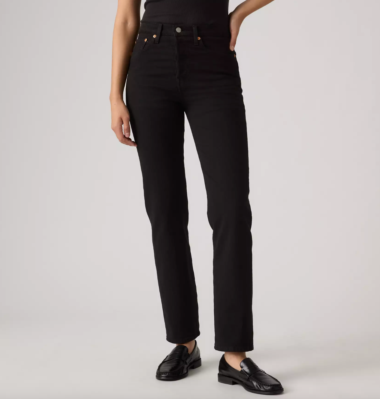 A model wearing black high-waisted straight-leg jeans and black leather loafers, shown from the waist down against a light gray studio background.