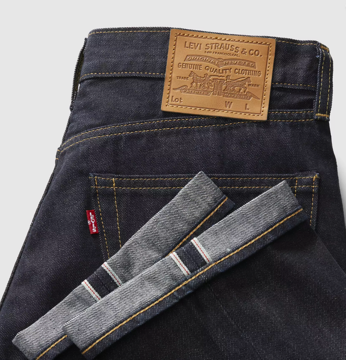 Close-up of the back waistband of Levi's dark indigo denim jeans, showing the signature brown leather patch and the folded hem of the cuffed leg with its striped twill construction.