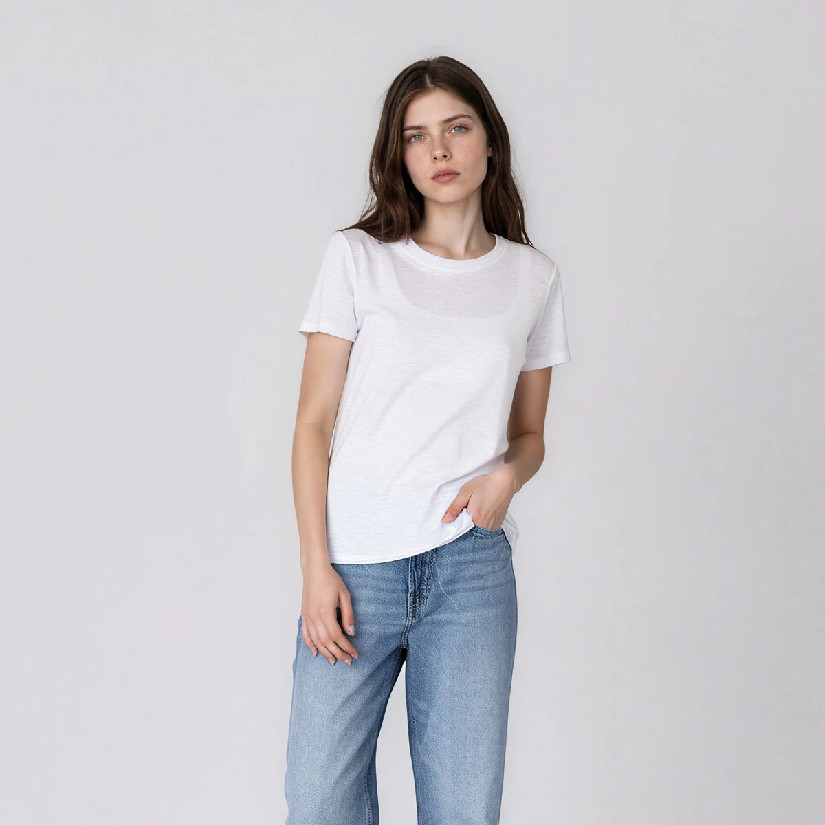 Model wearing It Is Well Everyday Crewneck Tee in Salt, full front view against light grey background showing crisp white lightweight slub jersey, crew neck, short sleeves with slight cuff, and relaxed full-length fit, styled with light wash wide-leg jeans and taupe Birkenstock slide sandals, hand in pocket

