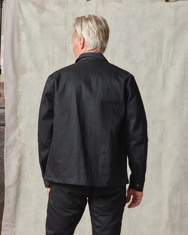 Model wearing the Tellason Coverall Jacket in Black Selvedge Denim buttoned up, styled with matching black selvedge denim pants, standing against a neutral backdrop