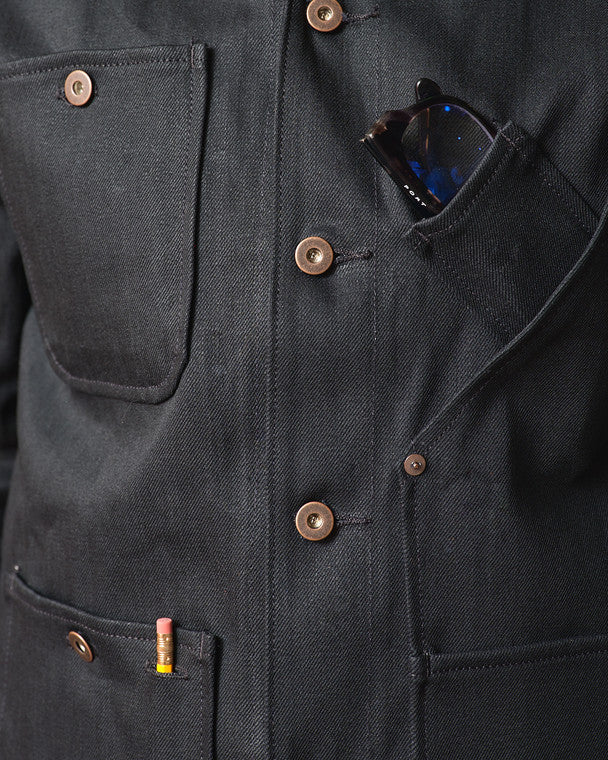 Close-up detail of the Tellason Coverall Jacket in Black Selvedge Denim showing the chest pocket, angled interior pocket with sunglasses, copper buttons, and Tellason selvedge label on the lower pocket
