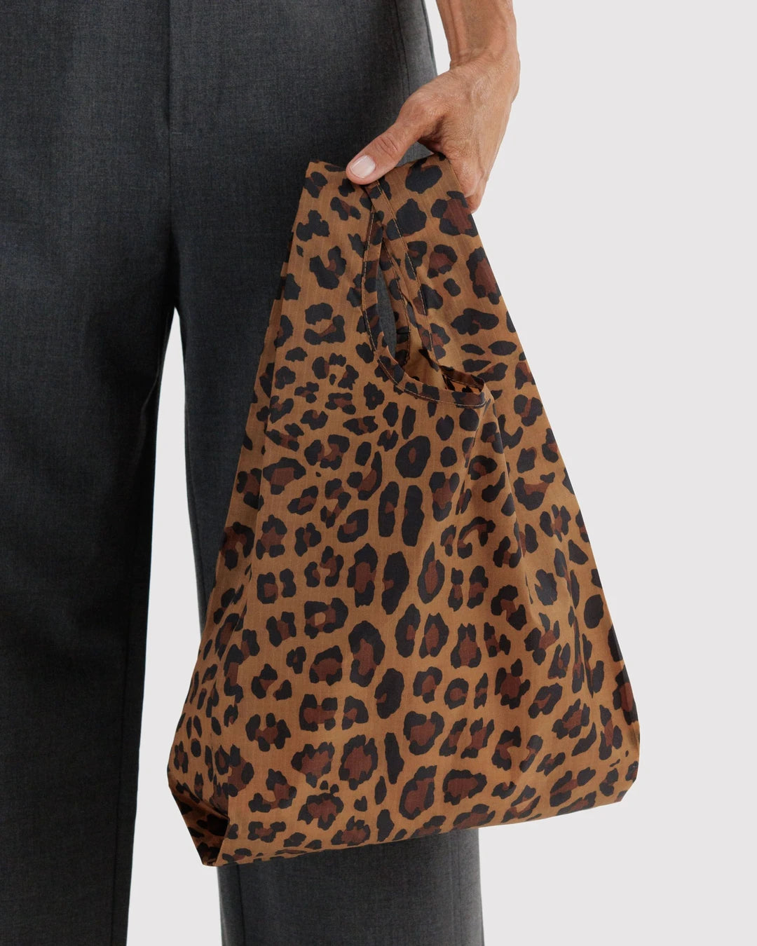 BAGGU Baby Baggu in Leopard, held at a model’s side to show the small tan shopping bag with brown and black leopard spots.