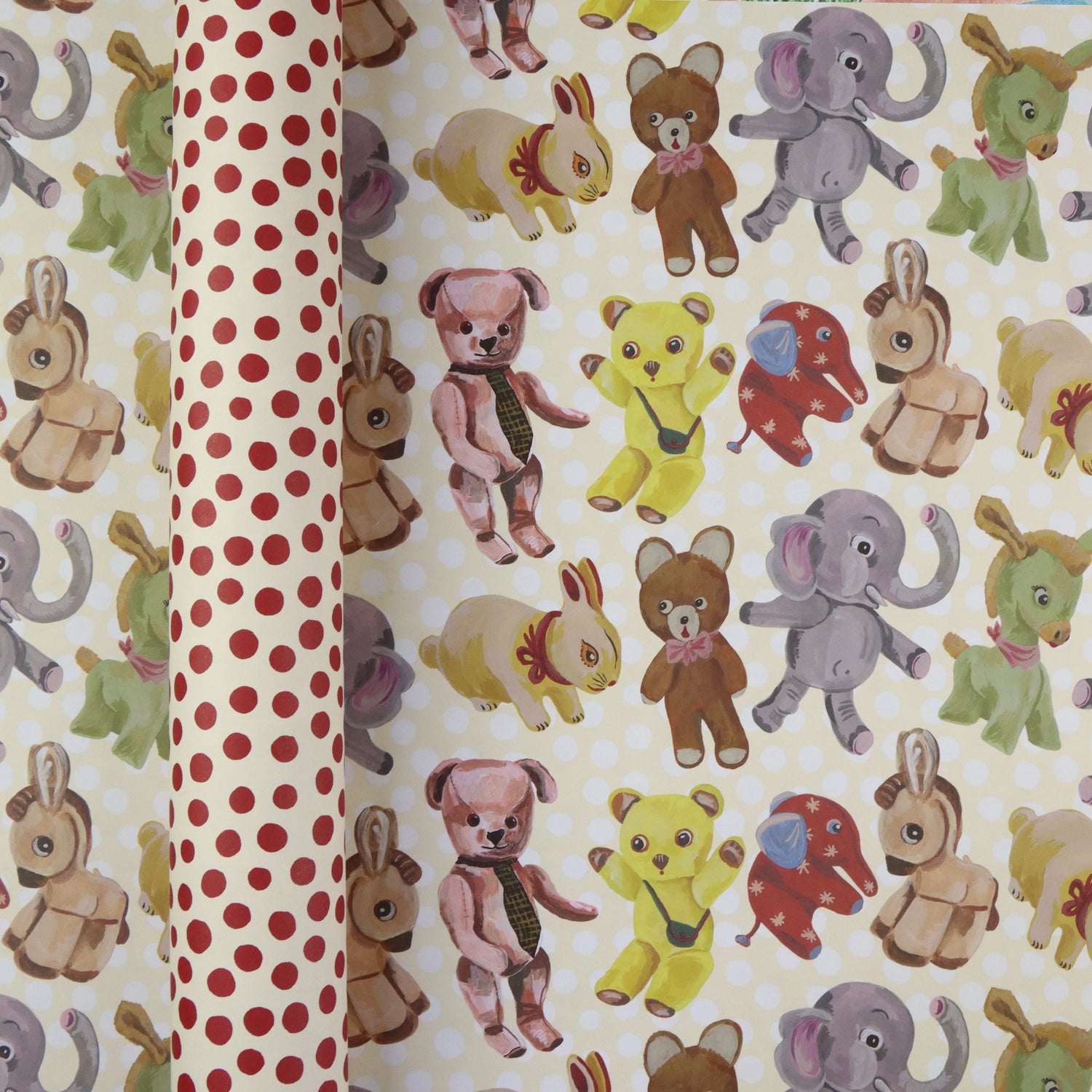  Plushies wrapping paper by Nathalie Lété shown rolled and flat, displaying vintage-style illustrated plush animals including teddy bears, elephants, rabbits, and donkeys on a cream background, with the red polka dot reverse visible on the rolled tube