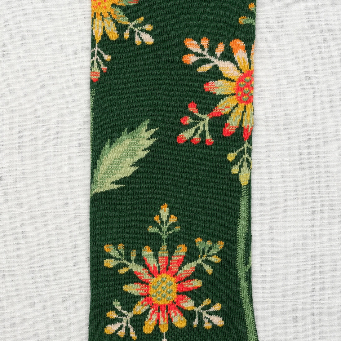 Bonne Maison Forest Snowflake Knee High Socks, close-up showing the botanical snowflake flower motifs in yellow, orange, and red with sage leaves on a forest green ground
