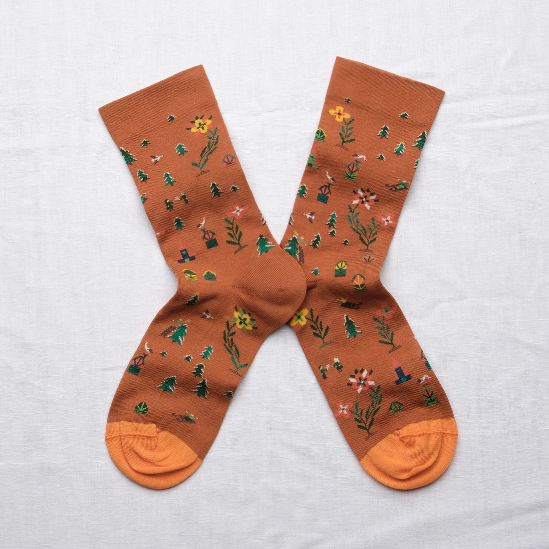 Bonne Maison Cinnamon Seed Socks, flat lay pair showing the cinnamon ground with scattered botanical print of pine trees, flowers, and plants in green, yellow, and pink
