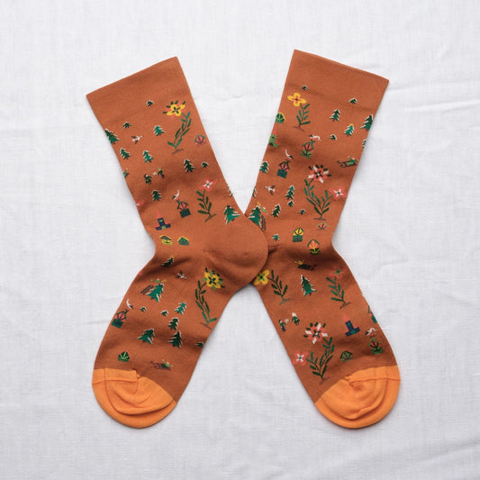 Bonne Maison Cinnamon Seed Socks, flat lay pair showing the cinnamon ground with scattered botanical print of pine trees, flowers, and plants in green, yellow, and pink
