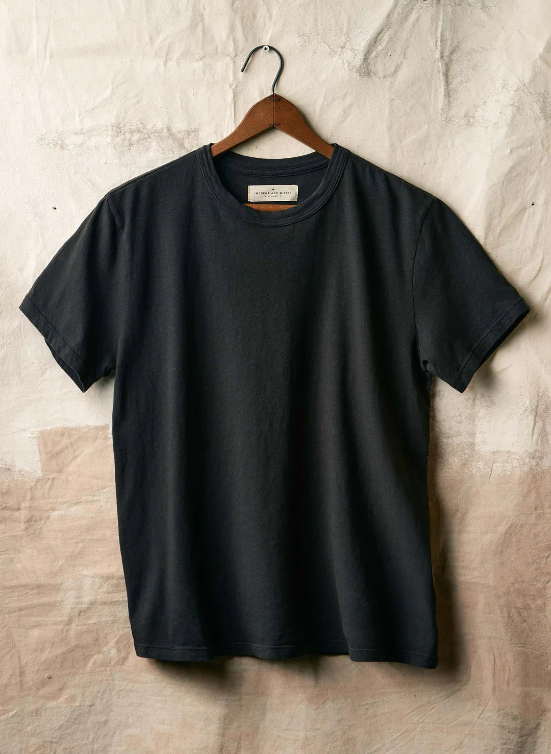 Imogene + Willie Classic Knit Crew in Black, short-sleeve crewneck t-shirt on a wooden hanger against a textured white backdrop — front view
