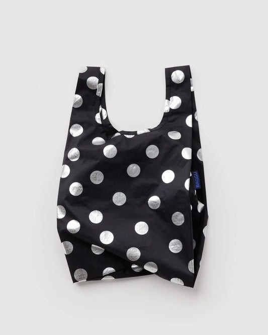 BAGGU Baby Baggu in Metallic Silver Polka Dot, shown unfolded with two handles and shiny silver dots on black fabric.
