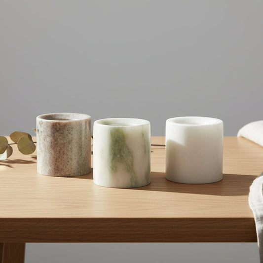Three marble-textured candle holders on a wooden table with a piece of eucalyptus resting on behind them