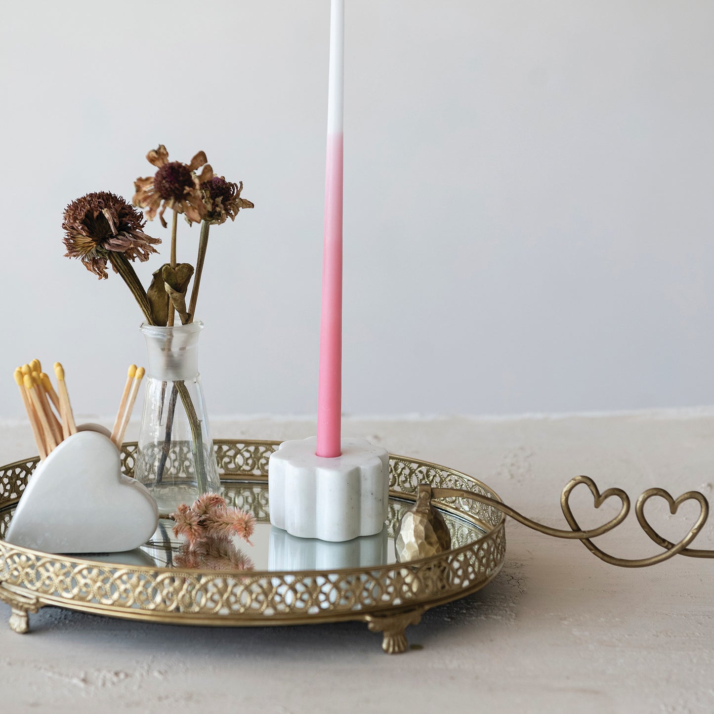 Decorative setup with a pink candle, heart-shaped objects, and a gold tray on a light surface.