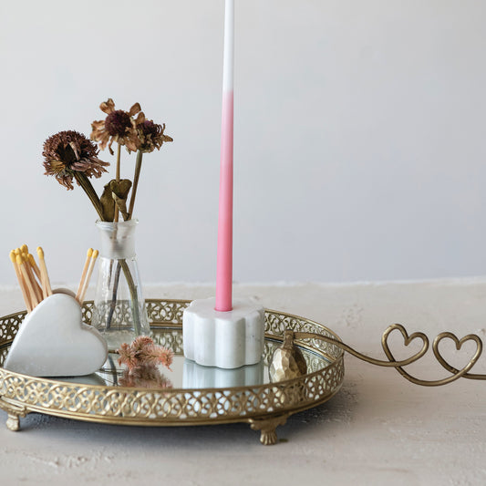 Decorative setup with a pink candle, heart-shaped objects, and a gold tray on a light surface.