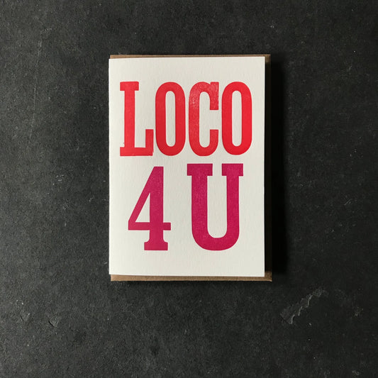 A square white art print or card with the words 'LOCO 4 U' in large red and magenta lettering, photographed from above on a dark textured surface.