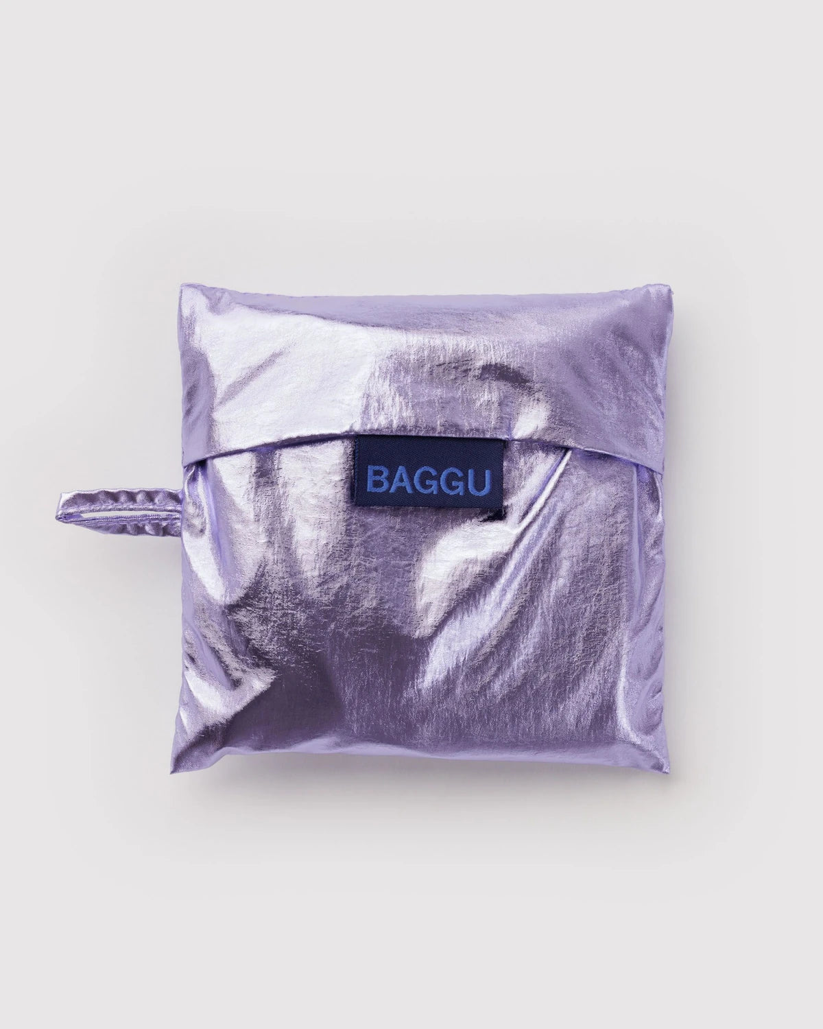 BAGGU Standard Baggu in Metallic Lavender, folded into its matching shiny lavender storage pouch with a visible BAGGU label.

