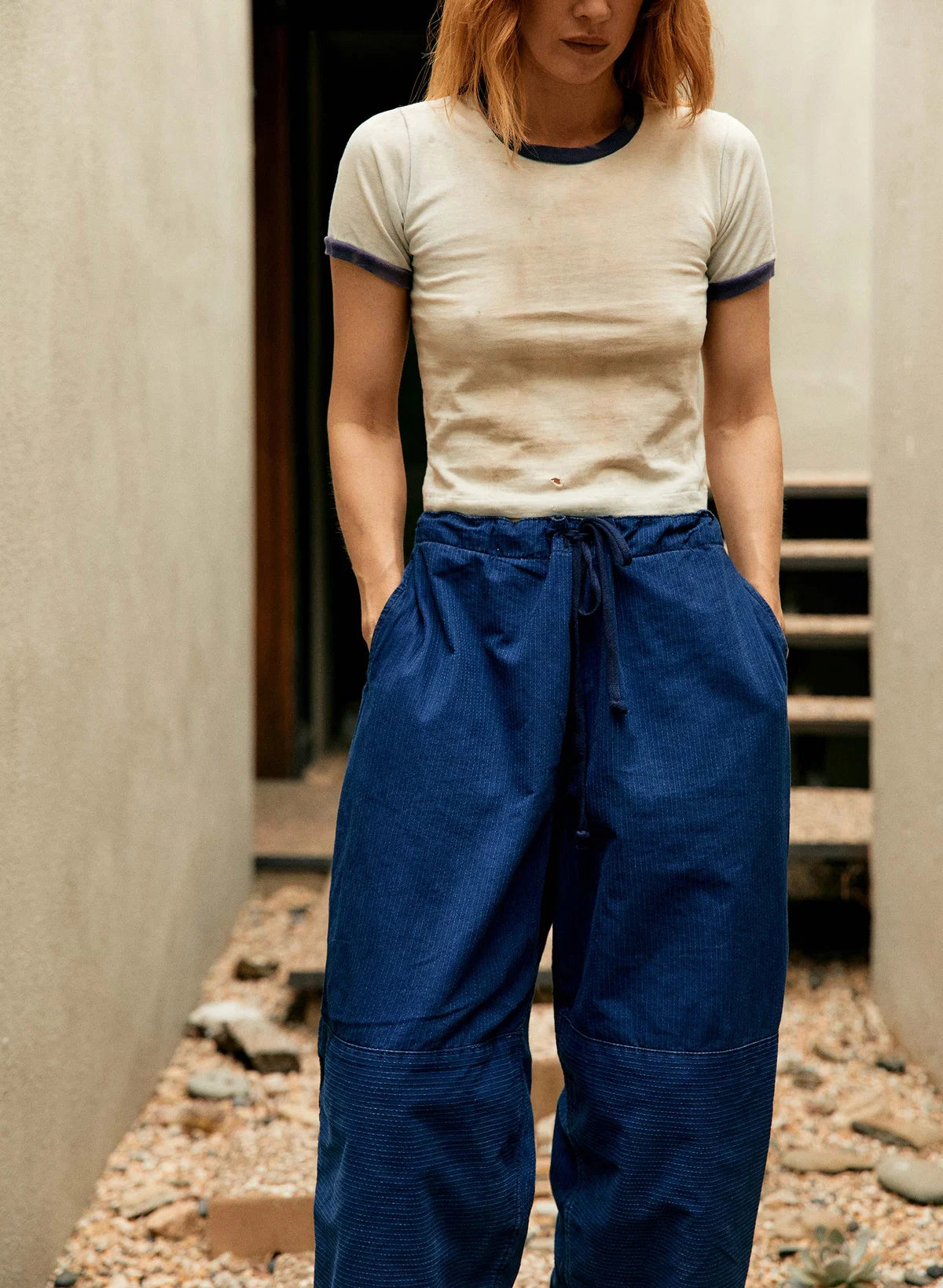 Front view of indigo sashiko flight pants with visible drawstring waist and double-knee detail, styled with a cream ringer tee.
