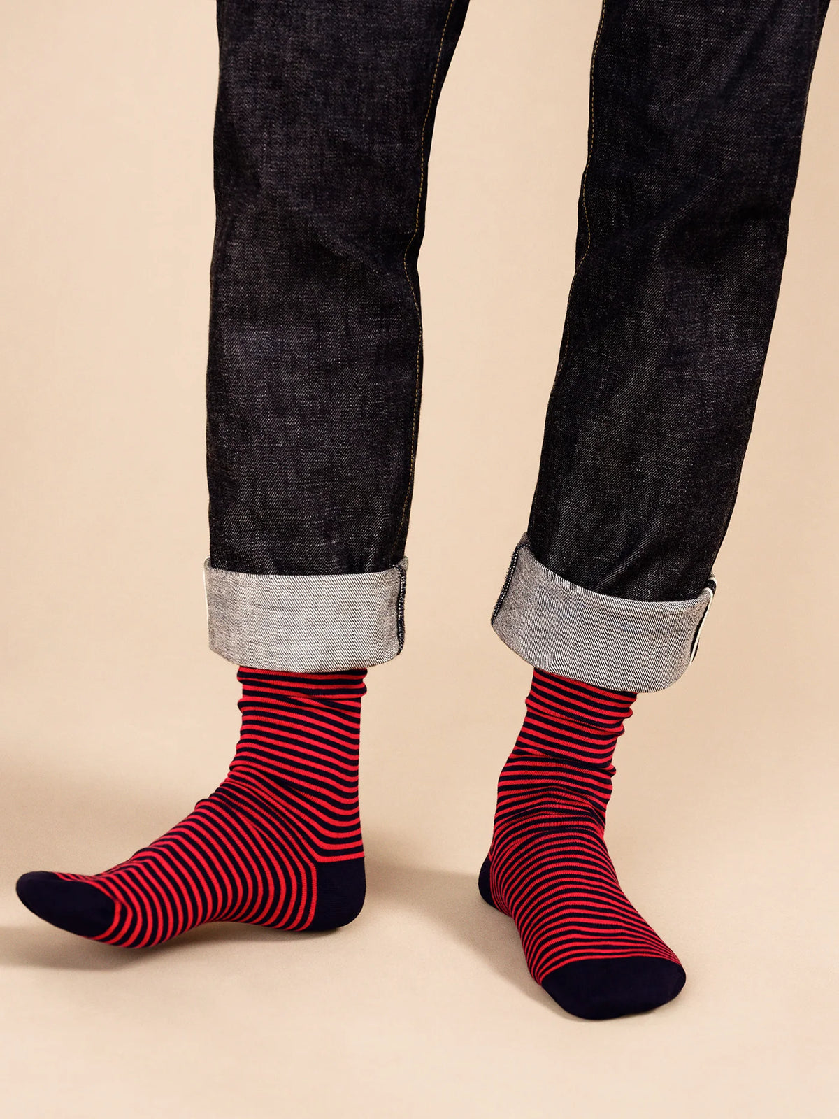 Model wearing navy and red striped crew socks with cuffed dark jeans, showing the solid navy heels and toes.
