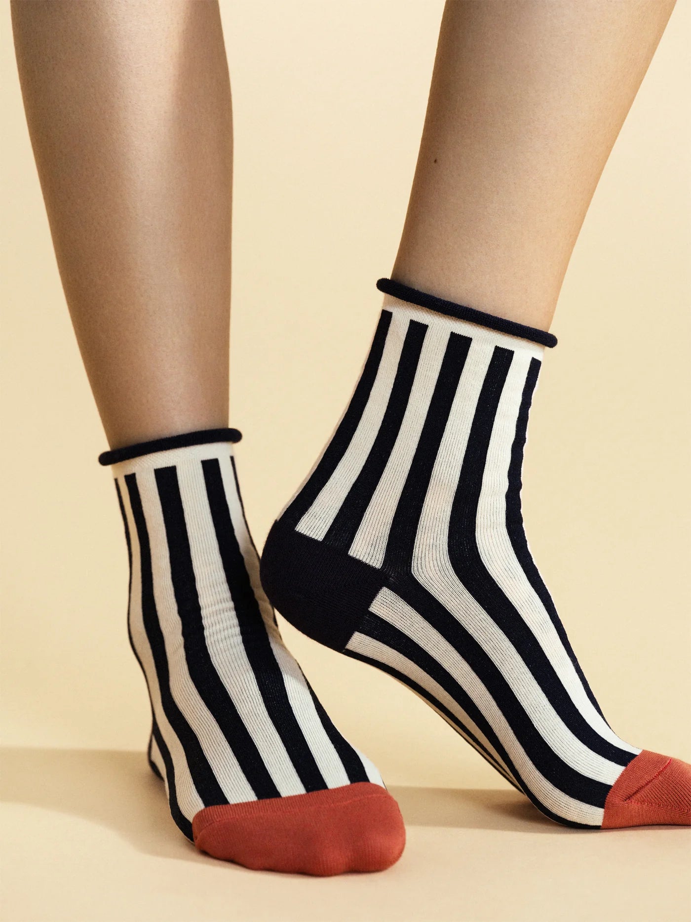 Black and white striped socks with red toes worn by a person on a beige background