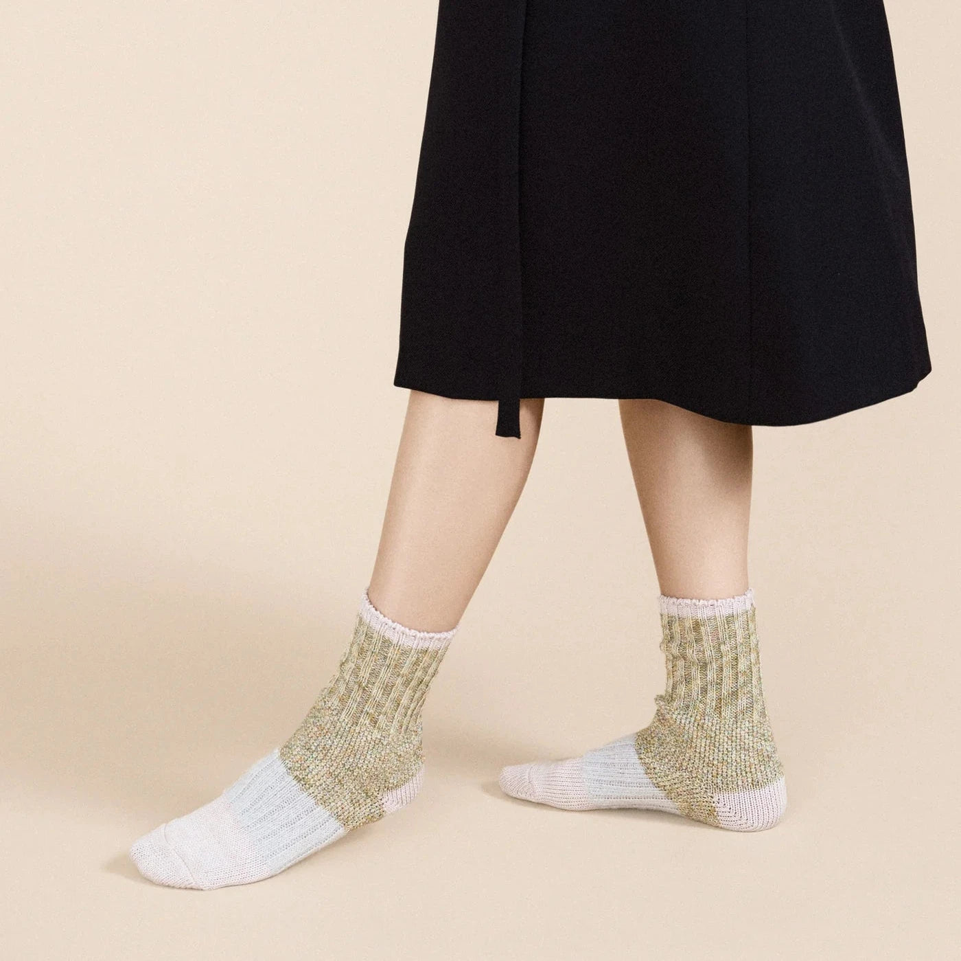 Pixie Dapple Crew socks in Pastel — sage and gold slub cotton crew with white heel and toe and pink rolled cuff, worn barefoot under a black midi skirt on a cream background
