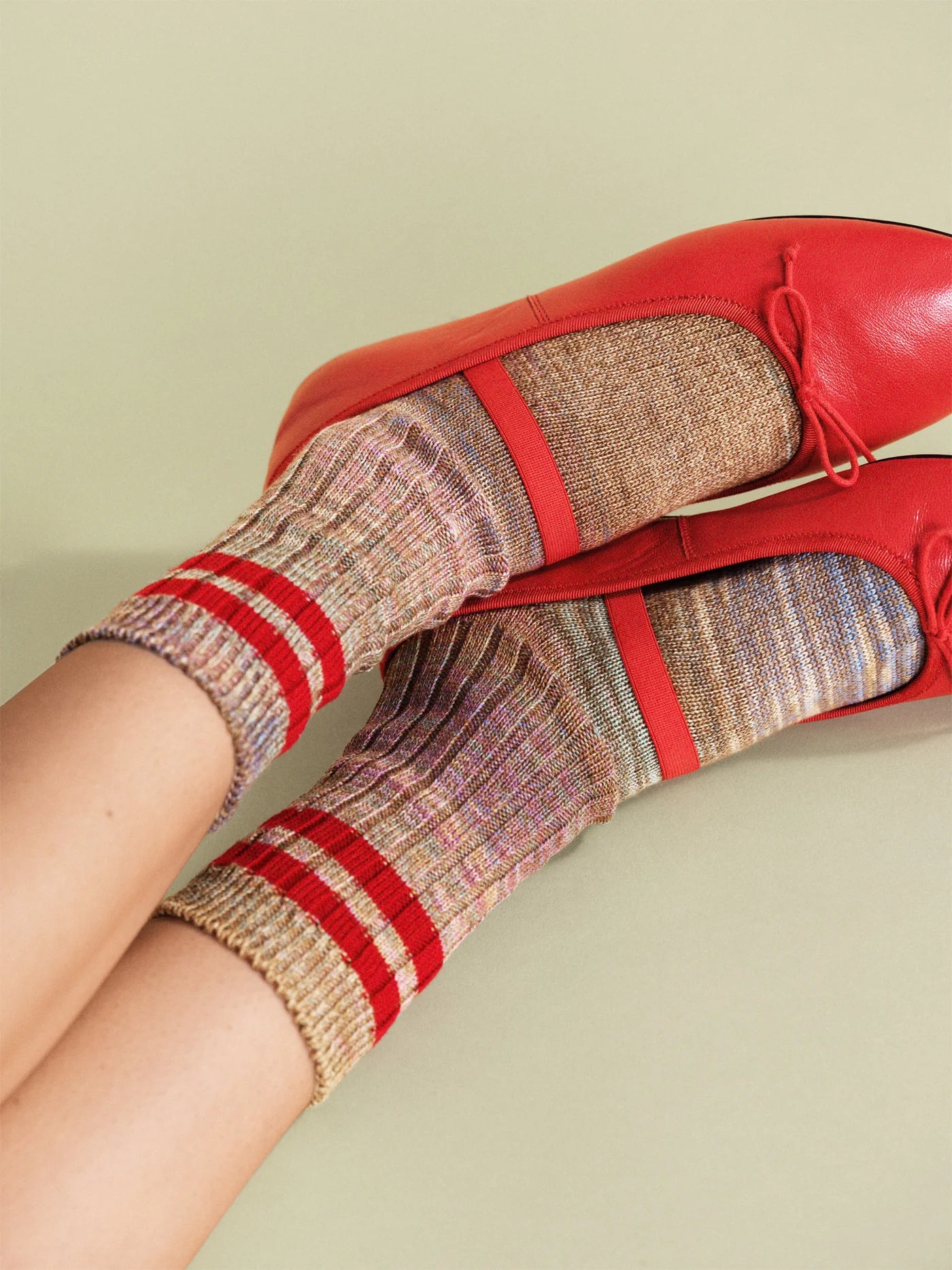 Cosmic Space Dye Varsity Crew socks in Ruby — multicolor space dye ribbed crew with bold red varsity stripes, worn with red leather bow ballet flats on a sage green background
