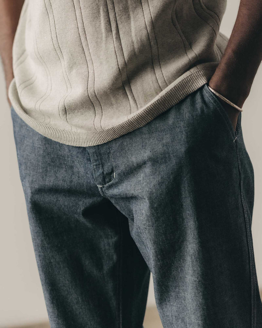Person wearing a beige sweater and dark jeans against a neutral background